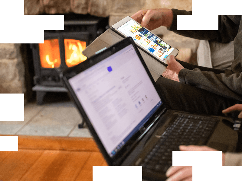 close up of two older people using laptop and tablet next to fireplace